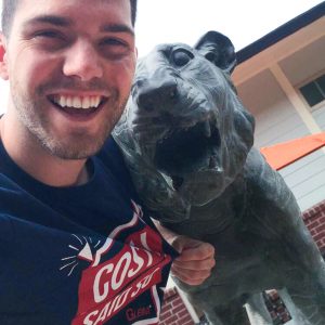 Austin, wearing his Gleim Campus Rep shirt, taking a selfie with a statue of LSU's mascot.